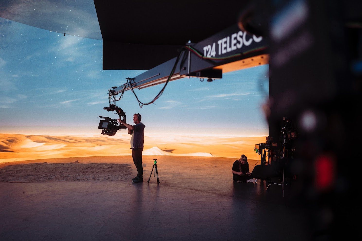 Operator adjusting a camera on a remote head in front of a virtual desert backdrop